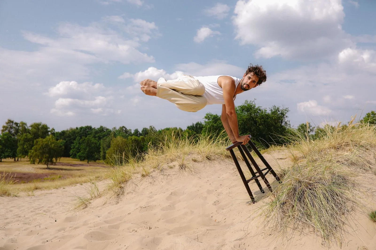 Philip Sergeychuck holding a planche on a stool on a sand dune